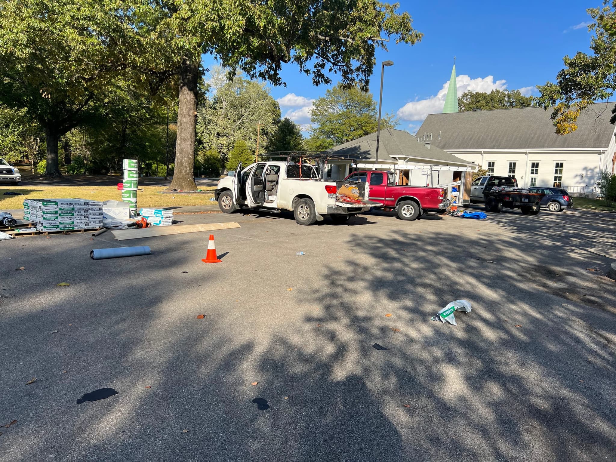 Roofing materials and work trucks staged in a church parking lot at the start of a re-roof