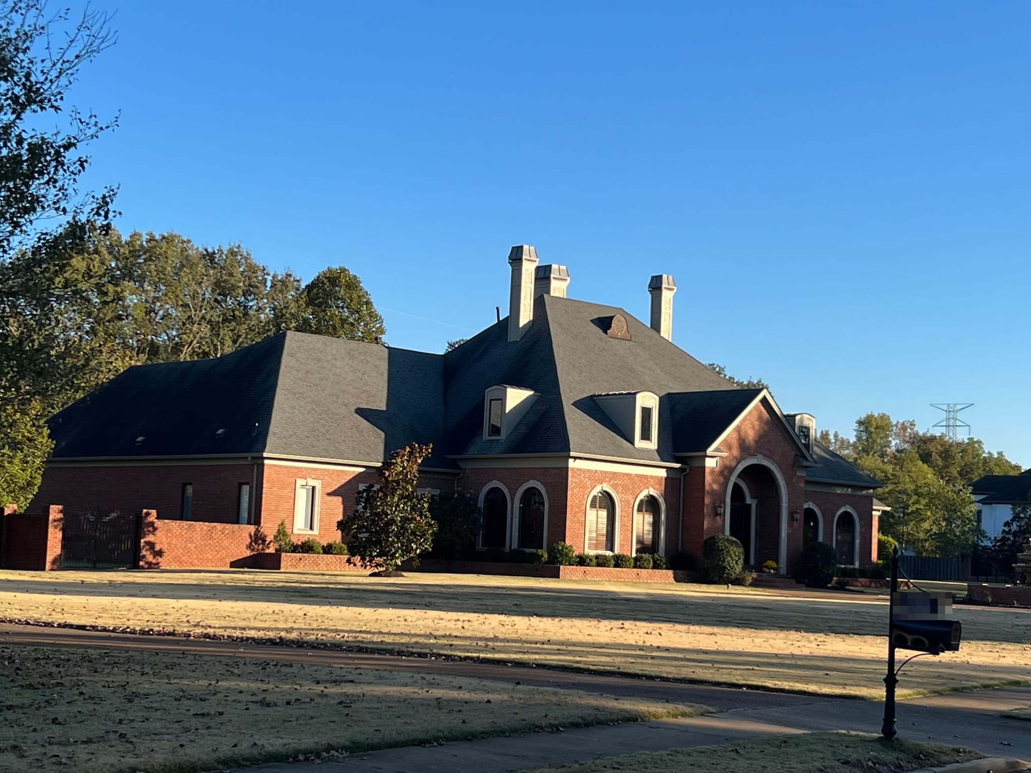 Side view of the red brick home with its three chimneys and existing dark grey roof before replacement