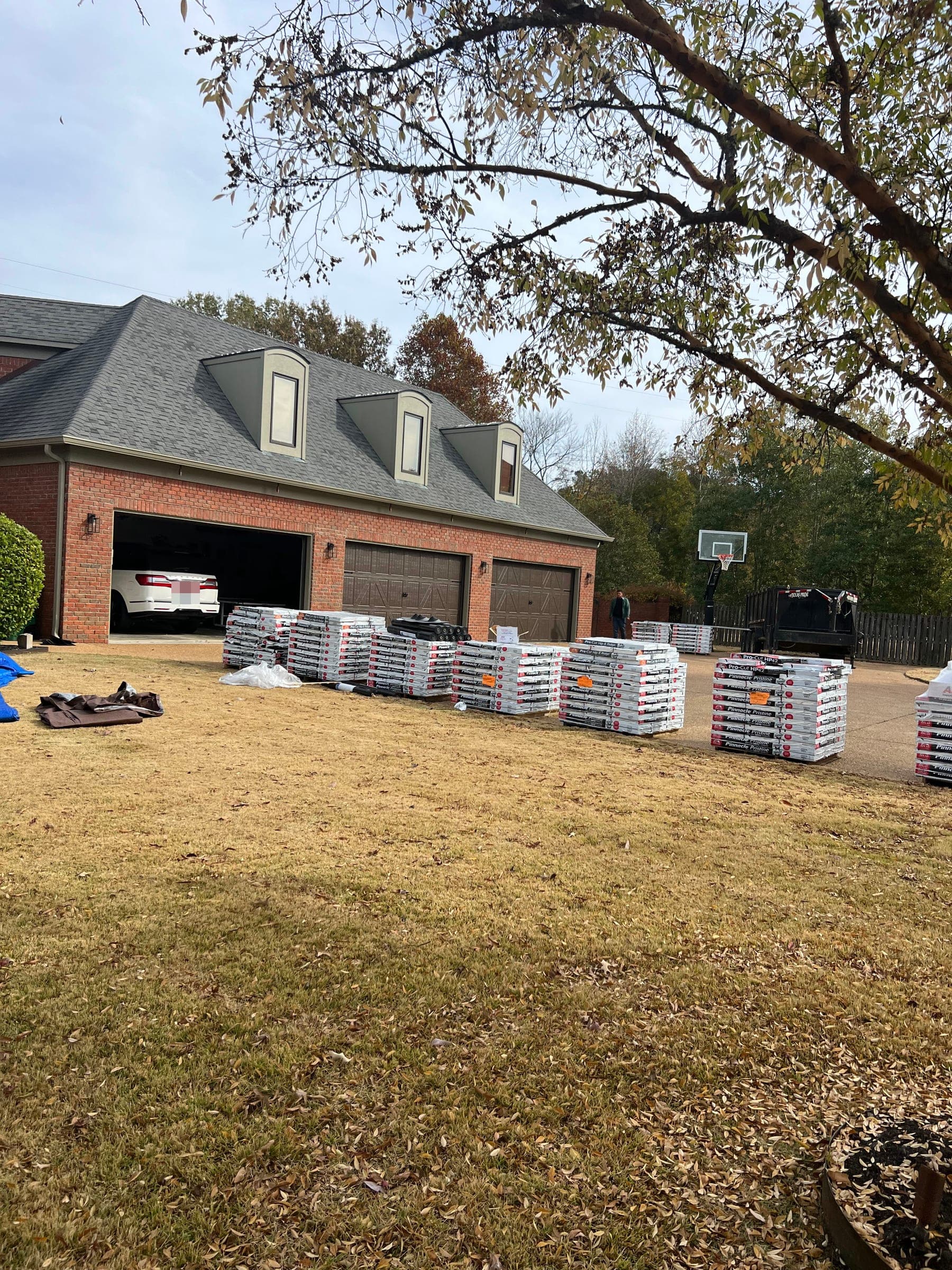 Pallets of Atlas Pinnacle Pristine shingles staged on the lawn in front of a brick home's three-car garage