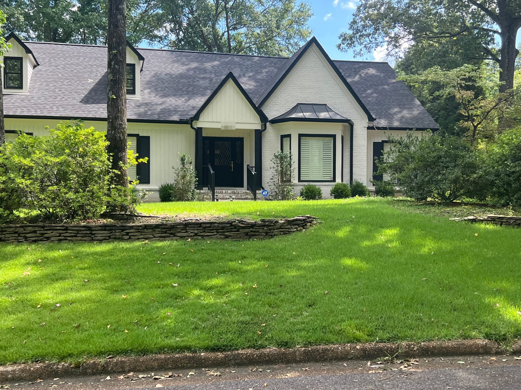 White brick and board-and-batten home with black trim, a charcoal shingle roof and a black standing-seam metal bay-window roof