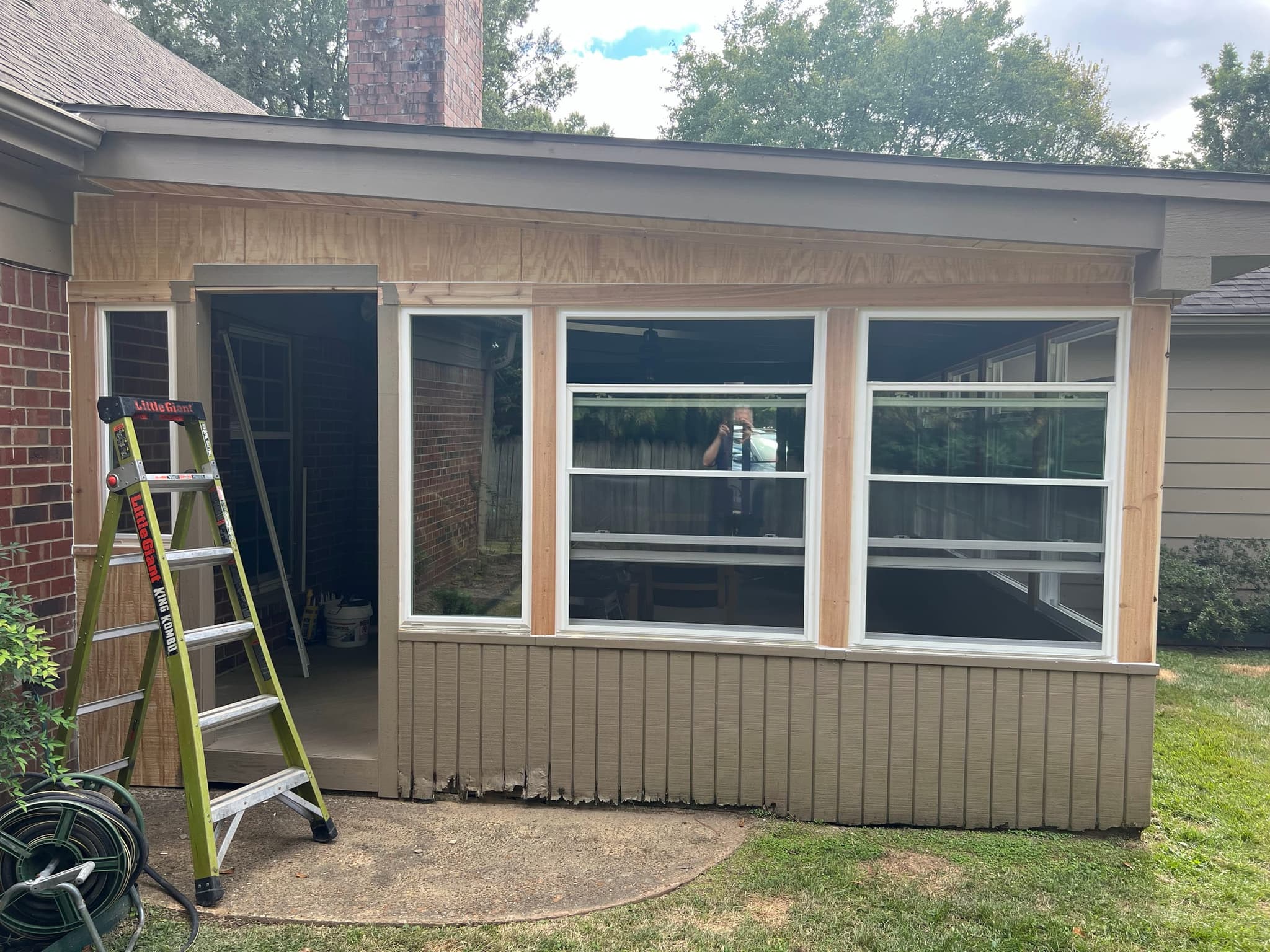 Outside the sunroom conversion: window frames installed, a ladder at the open doorway and a garden hose coiled on the ground